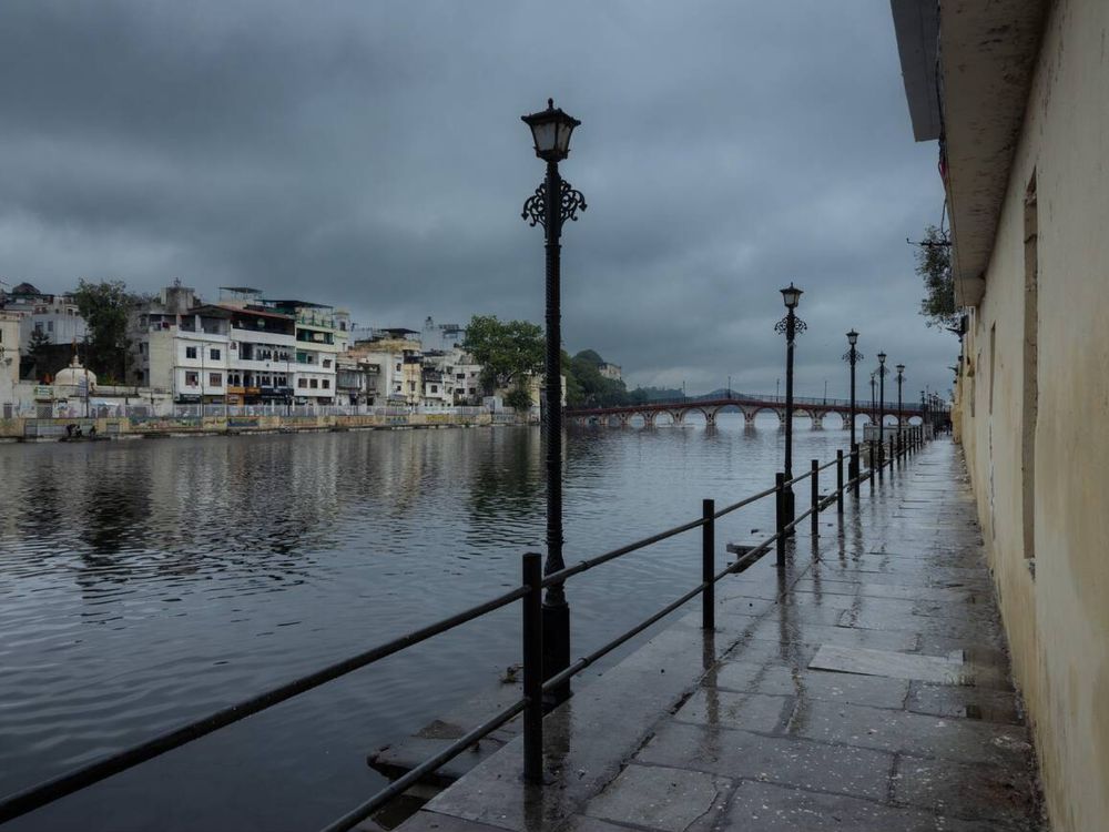 Wet lakeside walkway with lampposts along the shore of Lake Pichola in Udaipur on an overcast monsoon day