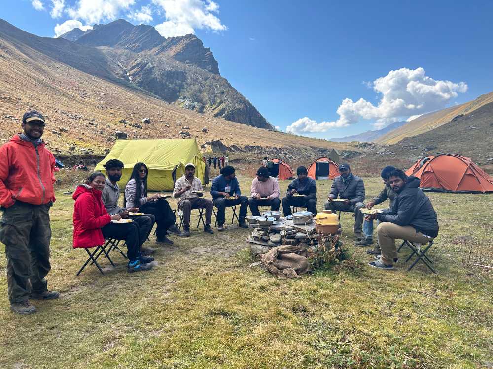 A group of people eating together, campsites behind them. 