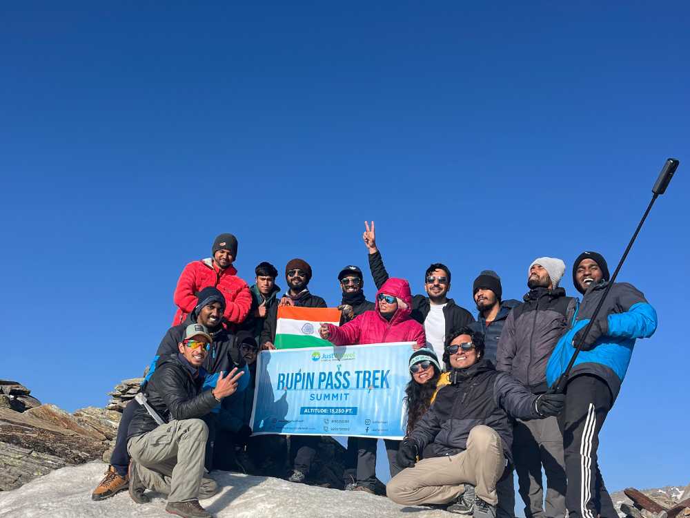 A group of people, standing with hands in the air, holding a banner on which Rupin Pass Summit is written. 