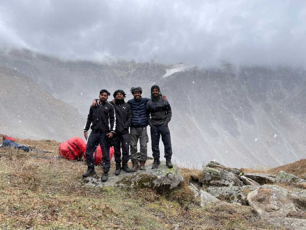 Four men standing at Buran Ghati, wearing woolen clothes, with mist surrounding them. 