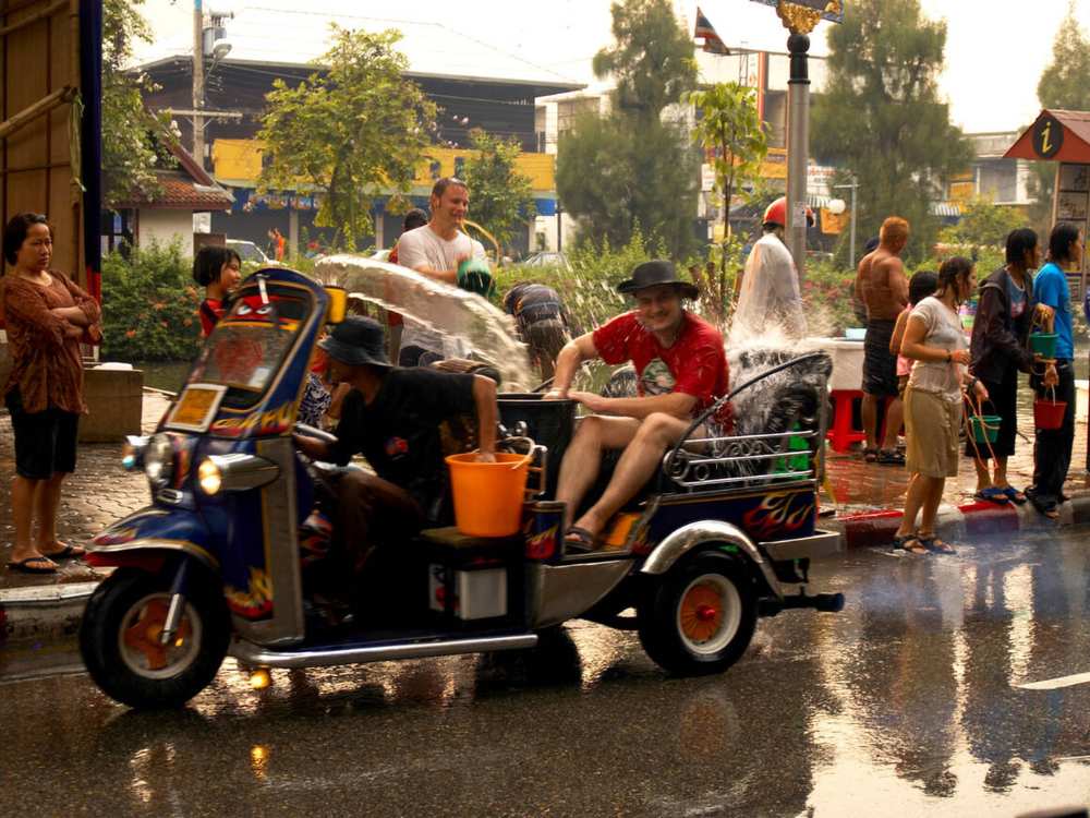 Tourists riding a tuk-tuk as locals splash water during Songkran celebrations