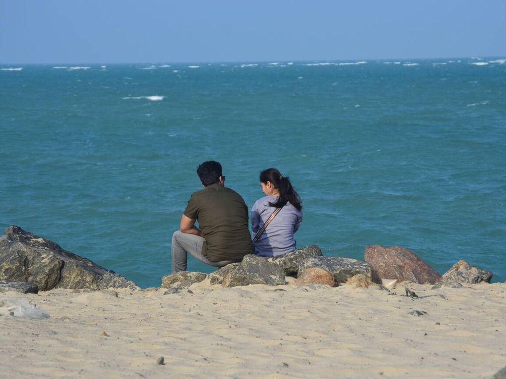 A couple is sitting at Dhanushkodi Beach in Tamil Nadu.